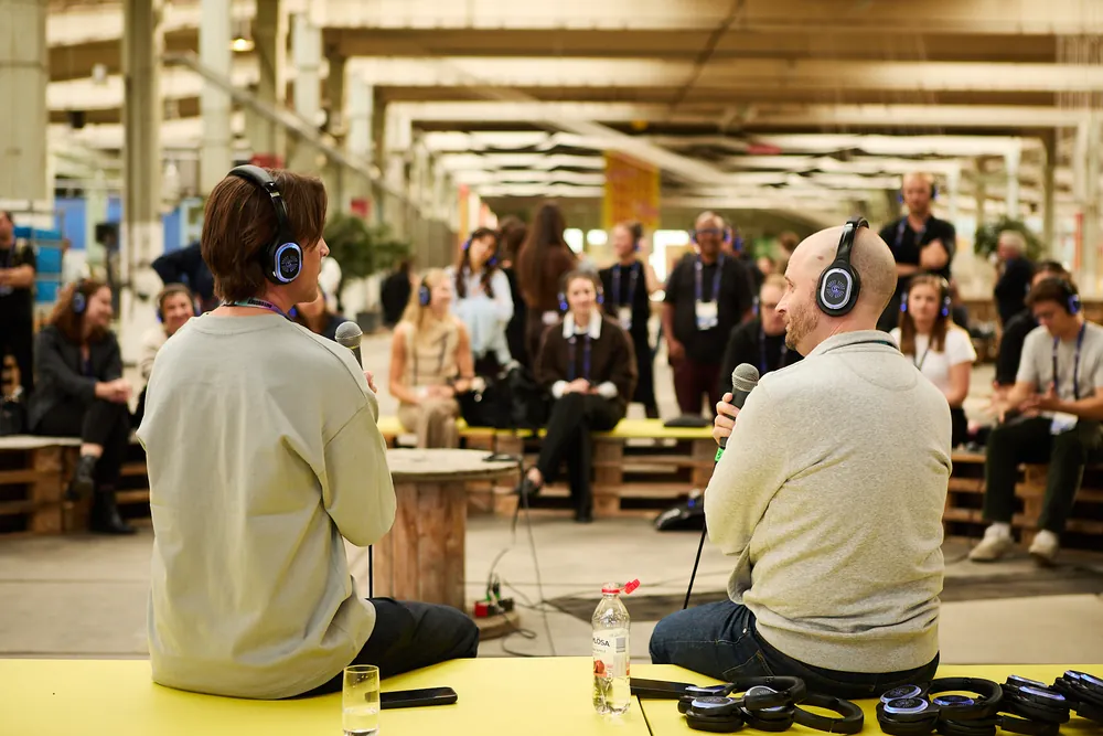 Two speakers in conversation on the yellow stage, the audience seated around them
